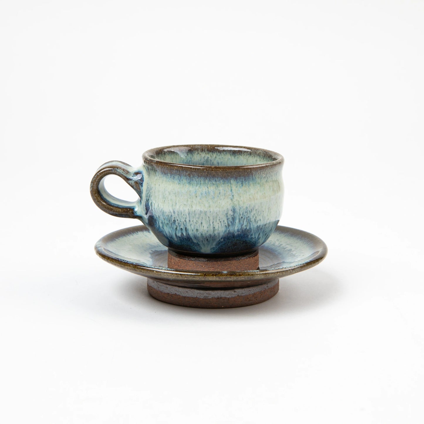 Side view of a blue and white glazed ceramic espresso cup with matching saucer, showcasing the rounded form and earthy base.