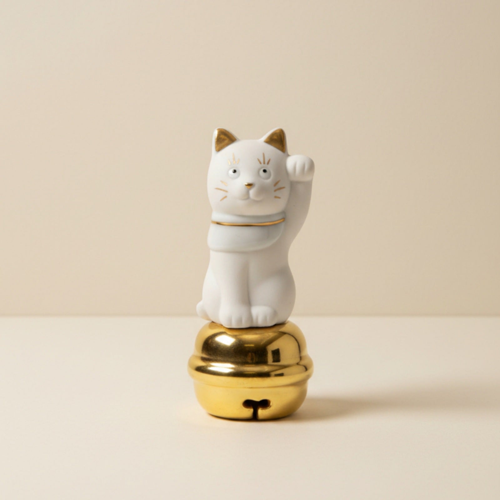 White cat figurine on a gold base against a beige background