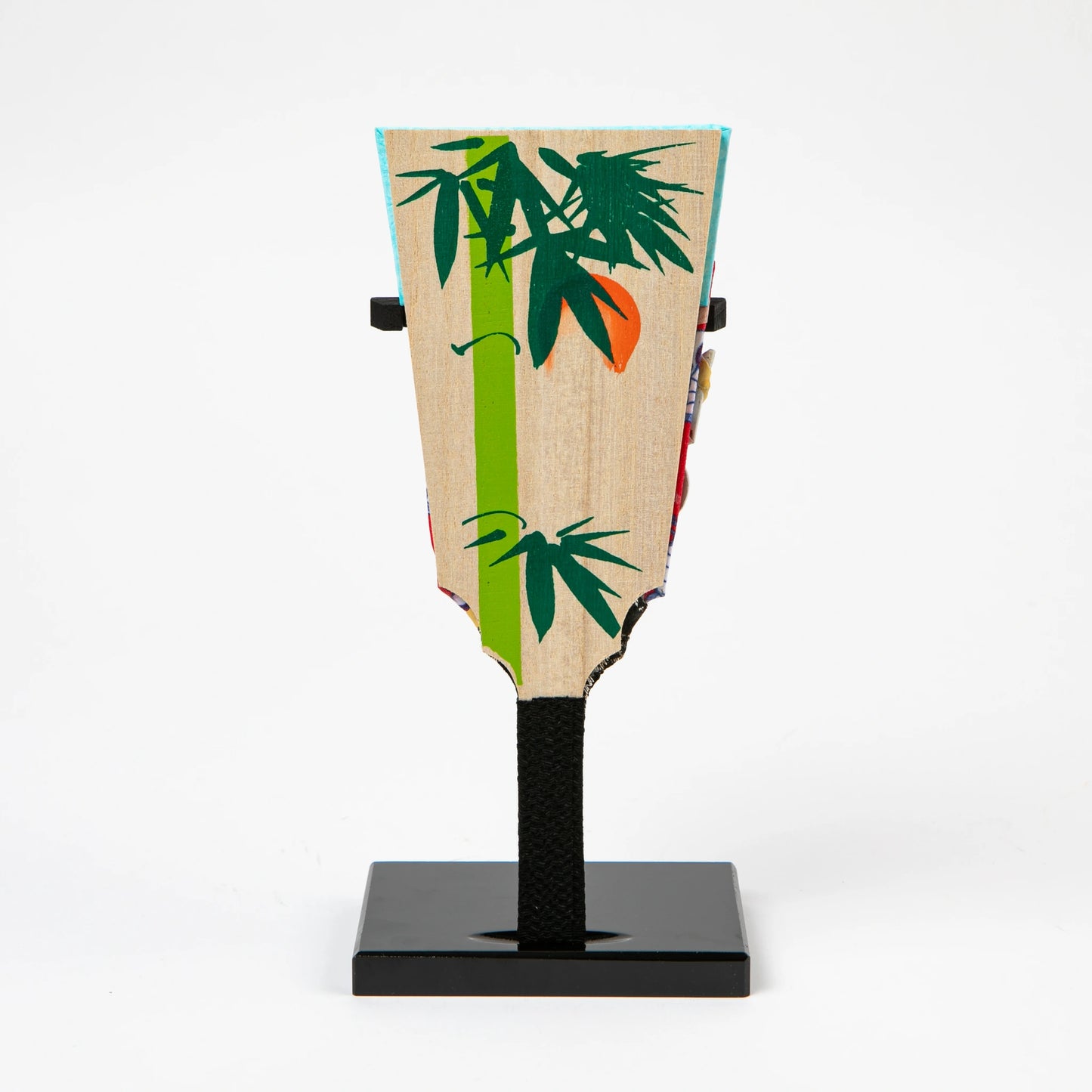 The reverse side of the decorative paddle, showcasing a natural wood grain background with a painted green bamboo and red sun motif.