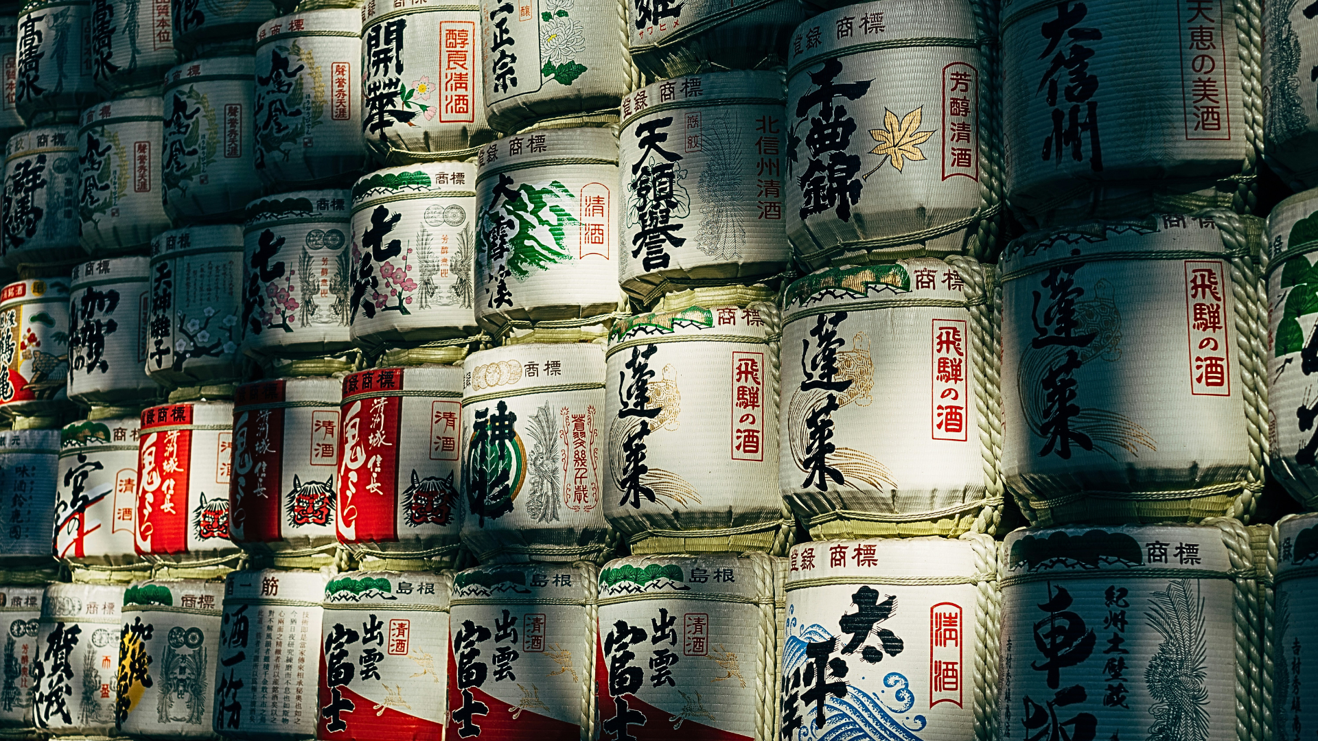Japanese sake barrels stored and stacked together outdoors with the sun beaming on it - Omakase