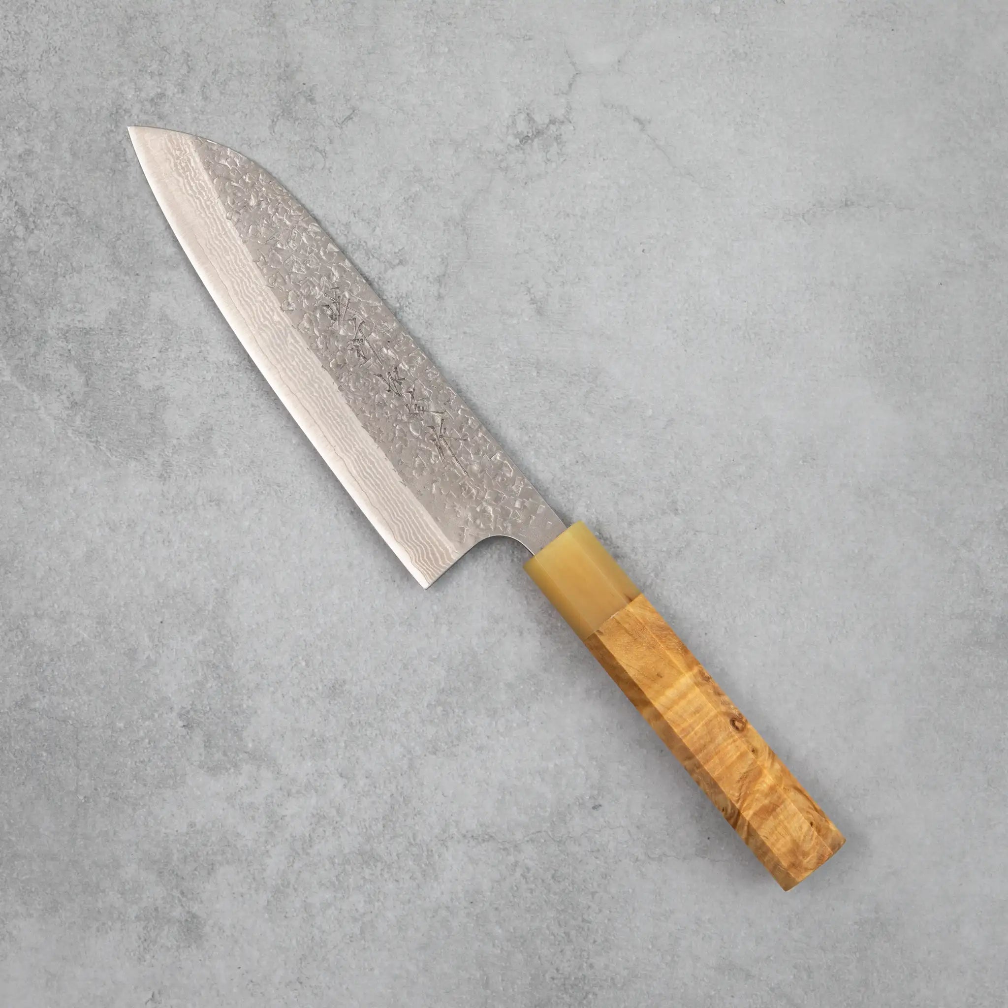 Side view of the Kamo Hamono Juhyo santoku knife, showing a VG10 Damascus blade with hammered tsuchime finish, a water buffalo horn bolster, and a stabilized figured wood handle with visible grain.