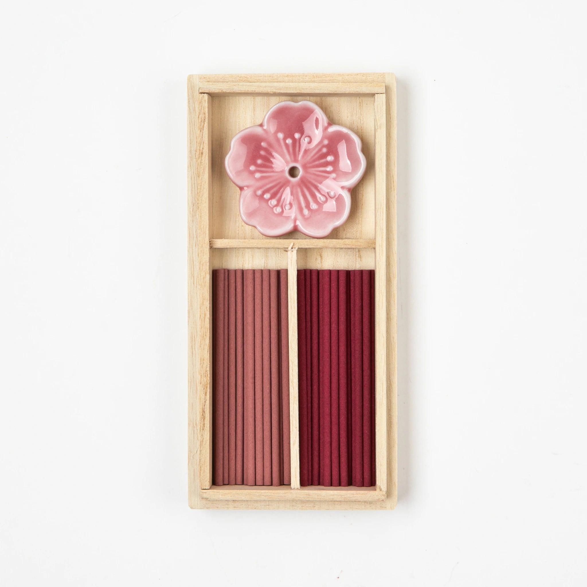 Open box of Japanese incense featuring pink and burgundy incense sticks and a cherry blossom-shaped ceramic holder.