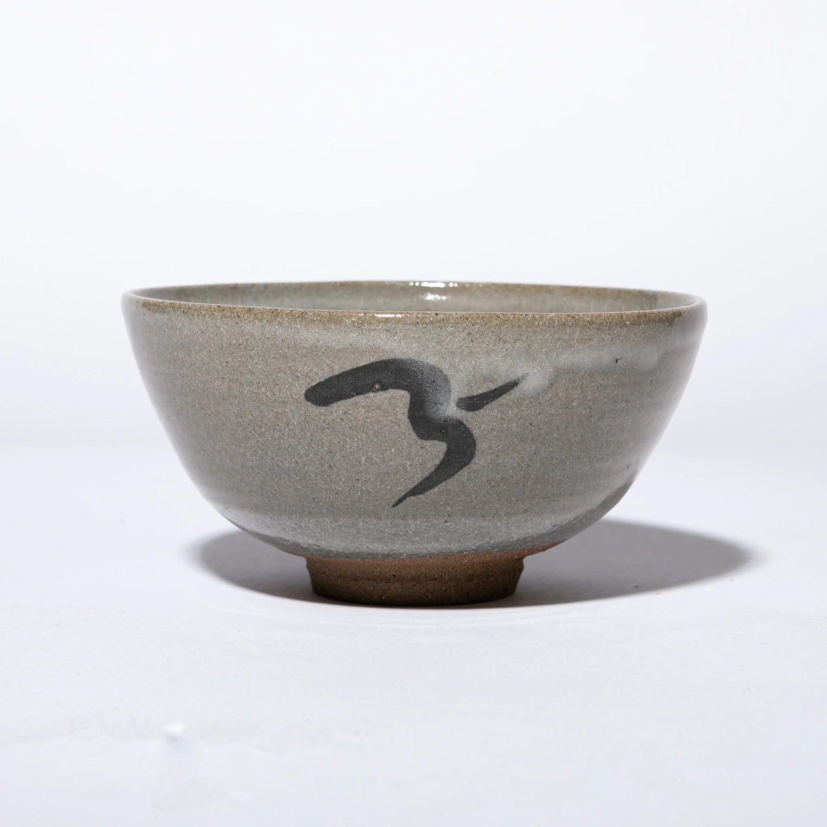 Front view of the Nakazato Tarouemon E-Karatsu matcha bowl with bird motif, showing a wide deep form with pale grey feldspathic glaze, an iron-oxide bird in flight painted on the exterior wall, and an unglazed sandy clay foot ring.