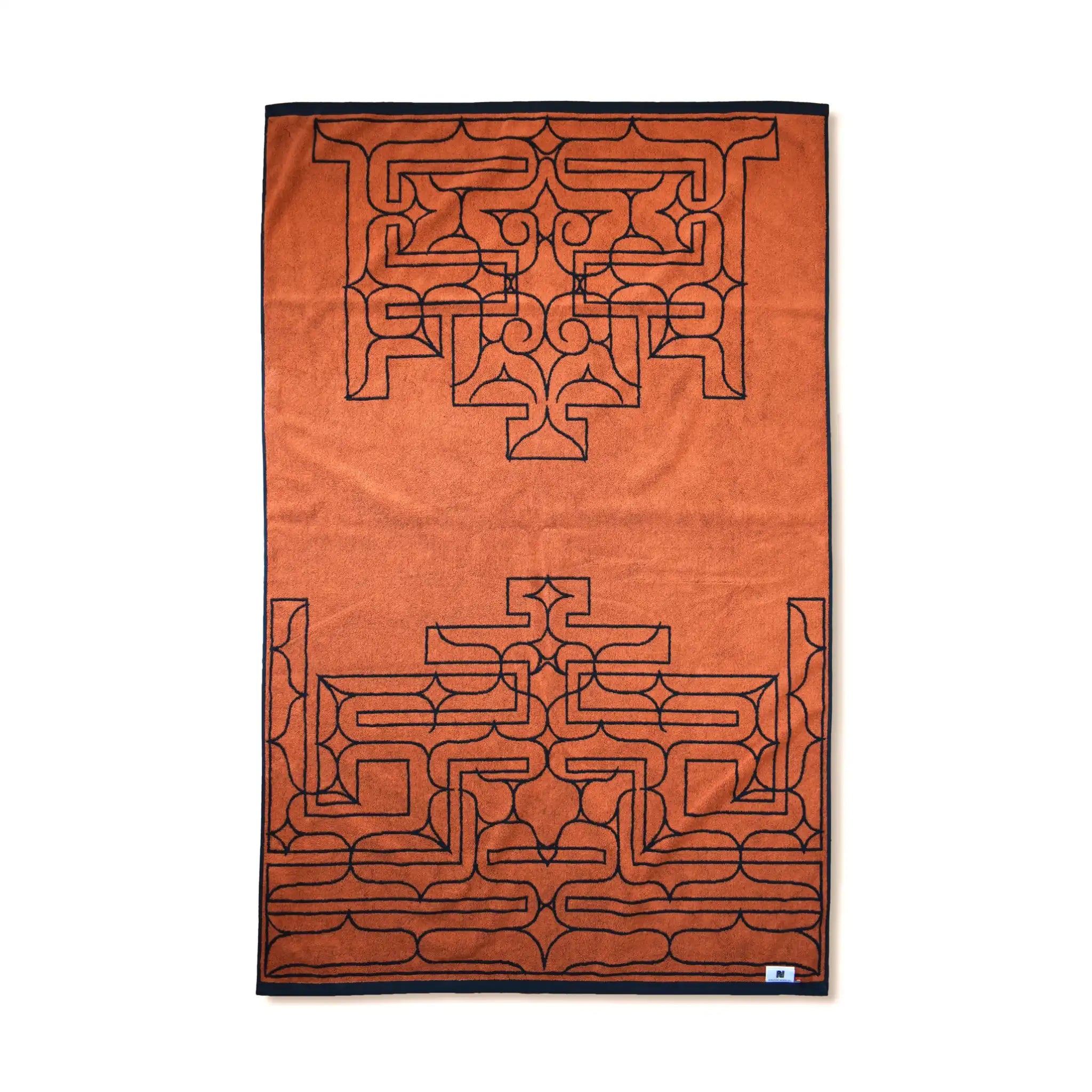 Reverse side of the Nibutani Works Ainu cikarkarpe pattern Imabari towel blanket showing orange ground with navy geometric pattern and navy border