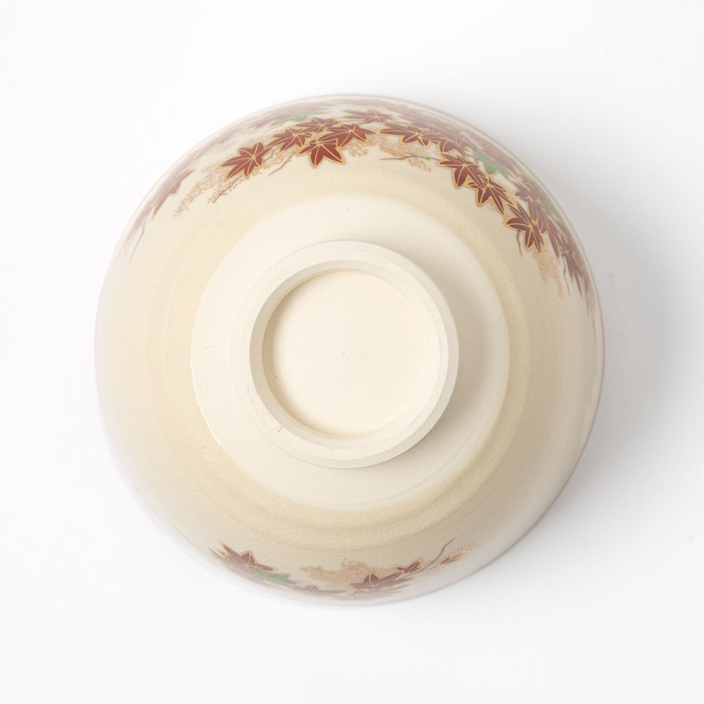 Underside view of a matcha bowl displaying a smooth, cream-colored base with a subtle maple leaf design on the upper part.