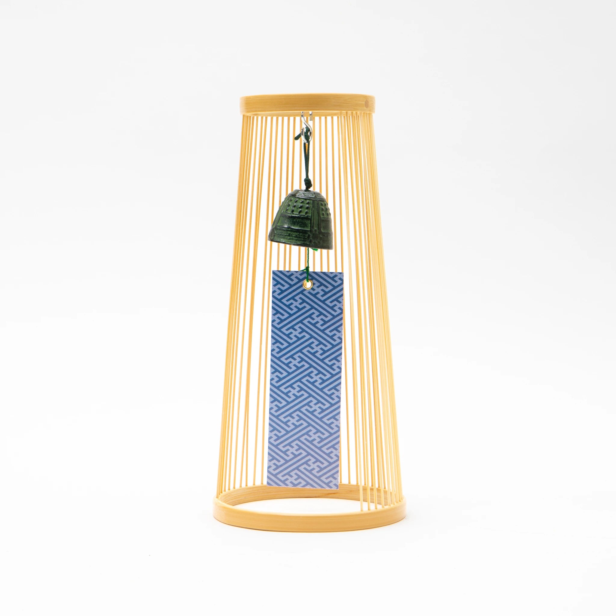 Front view of the Hatsukaze tabletop wind chime, showing a tapered cylindrical frame of fine pale Suruga bamboo strips between two circular rings, with a small dark cast bell suspended at center and a blue geometric patterned paper strip hanging below it.