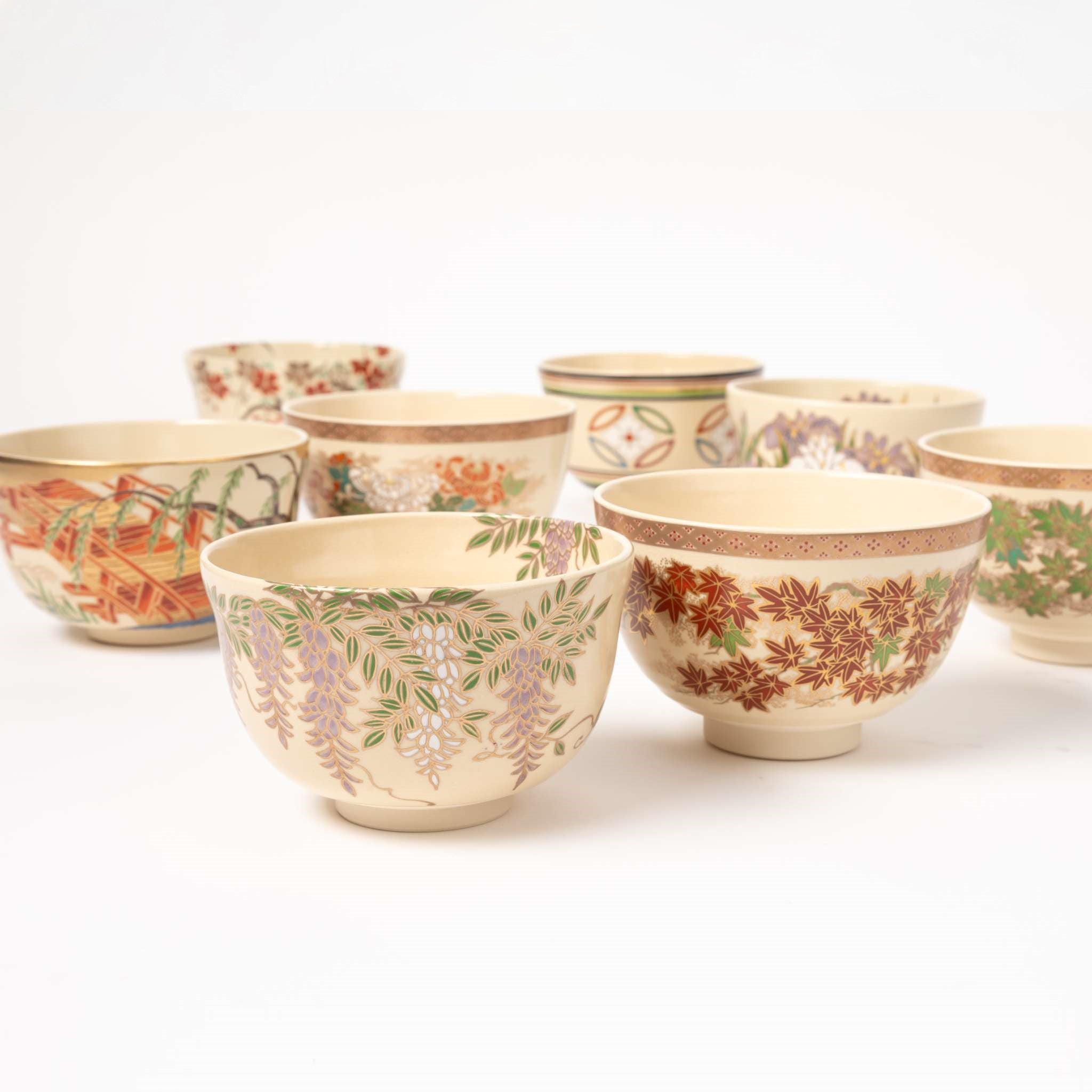 A collection of beautifully handcrafted matcha bowls by Eiko Miyaji, showcasing various intricate designs and patterns, including wisteria and red maple leaf motifs, arranged together in a visually appealing display.