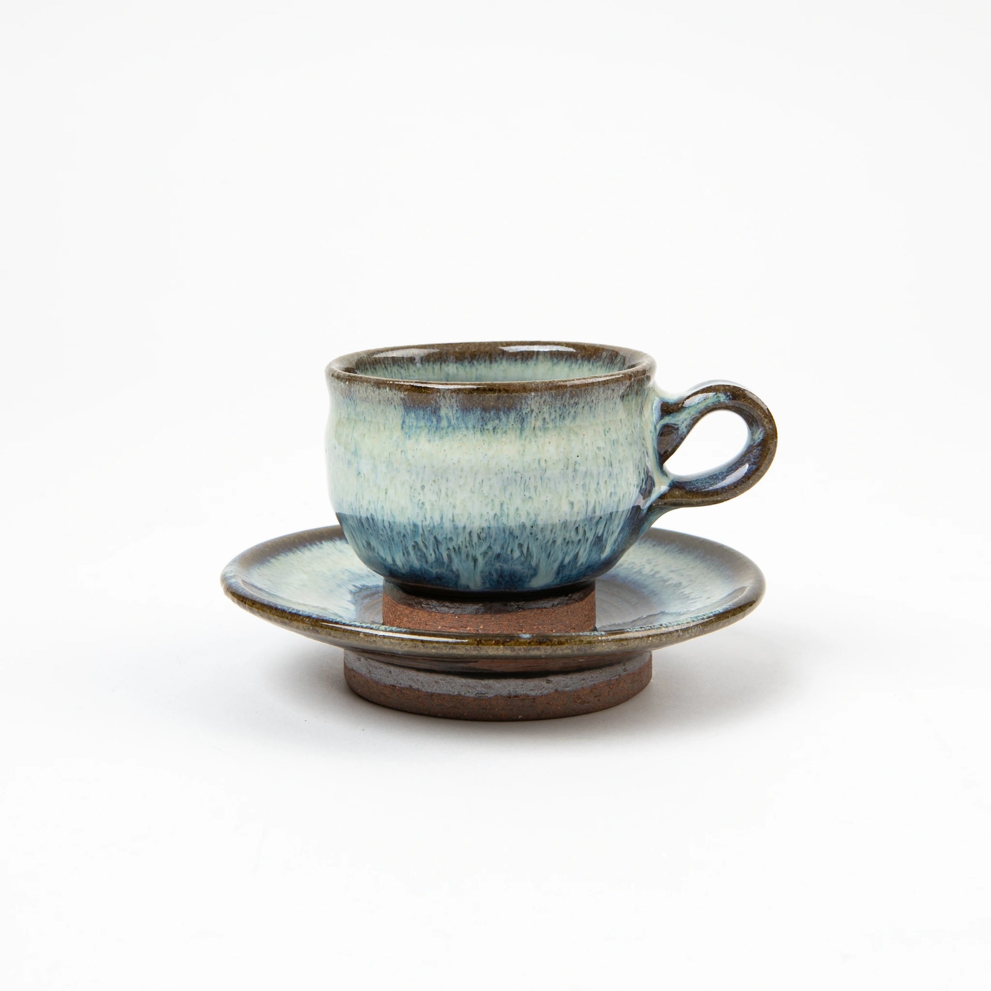 A hand-glazed ceramic espresso cup and saucer with layered blue and white tones, set on a white background.
