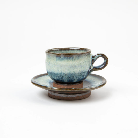 A hand-glazed ceramic espresso cup and saucer with layered blue and white tones, set on a white background.