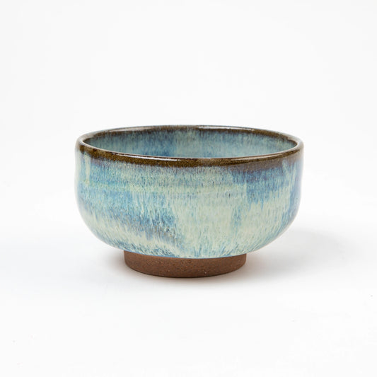 A handcrafted matcha bowl with a glossy blue and white drip glaze, shown against a white background.