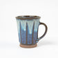 A ceramic mug with a flared rim and a vertical pattern of blue and white glaze over a dark brown base.
