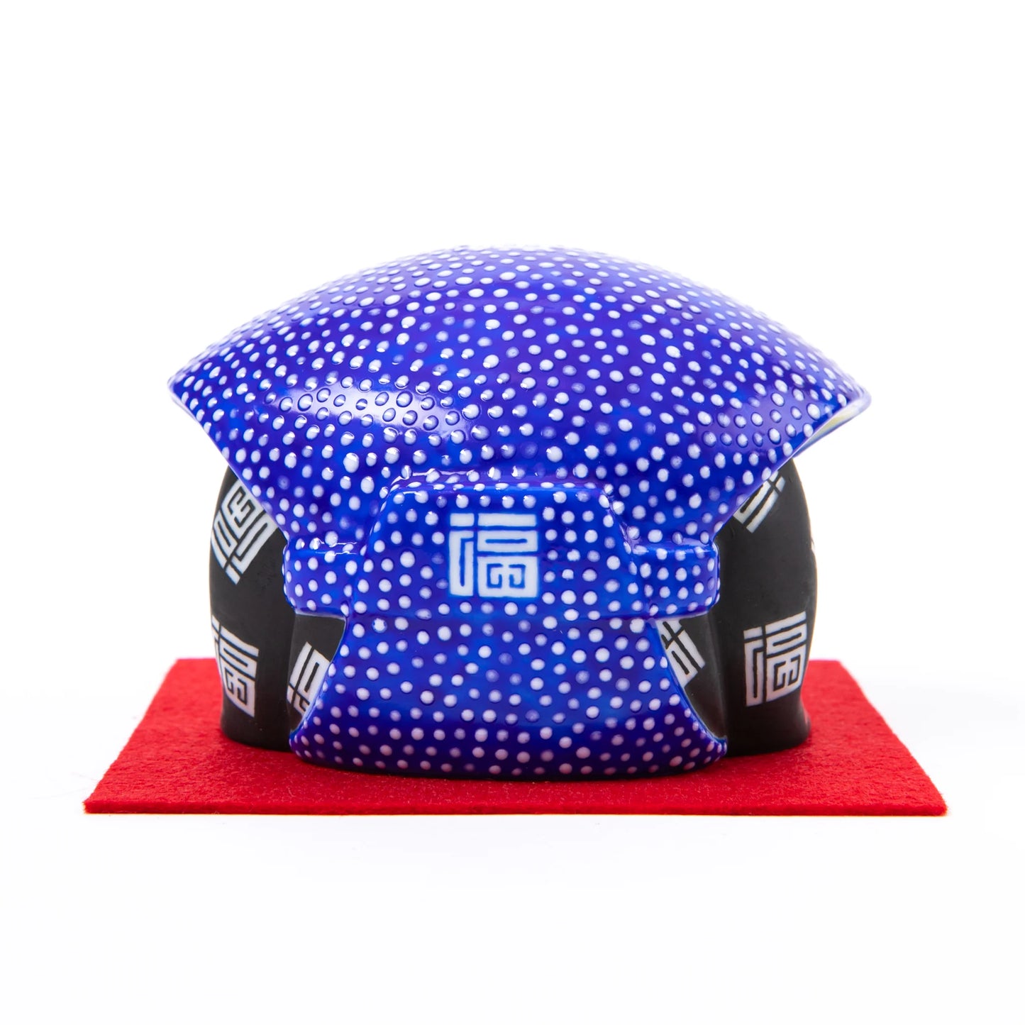 A rear view of the bowing Fukusuke doll, displaying the blue polka-dot headscarf and kanji characters on the kimono’s back, with its rounded shape prominent.