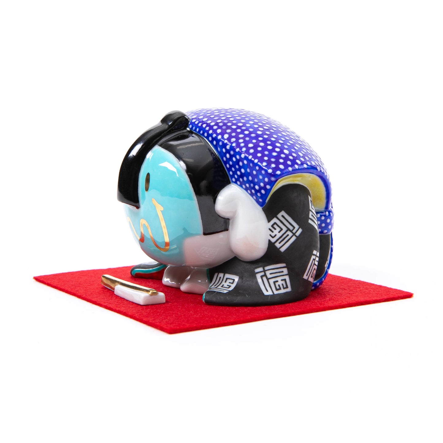 A different angled side view of the bowing Fukusuke doll, showcasing its intricate kimono design and a small decorative accessory in front.