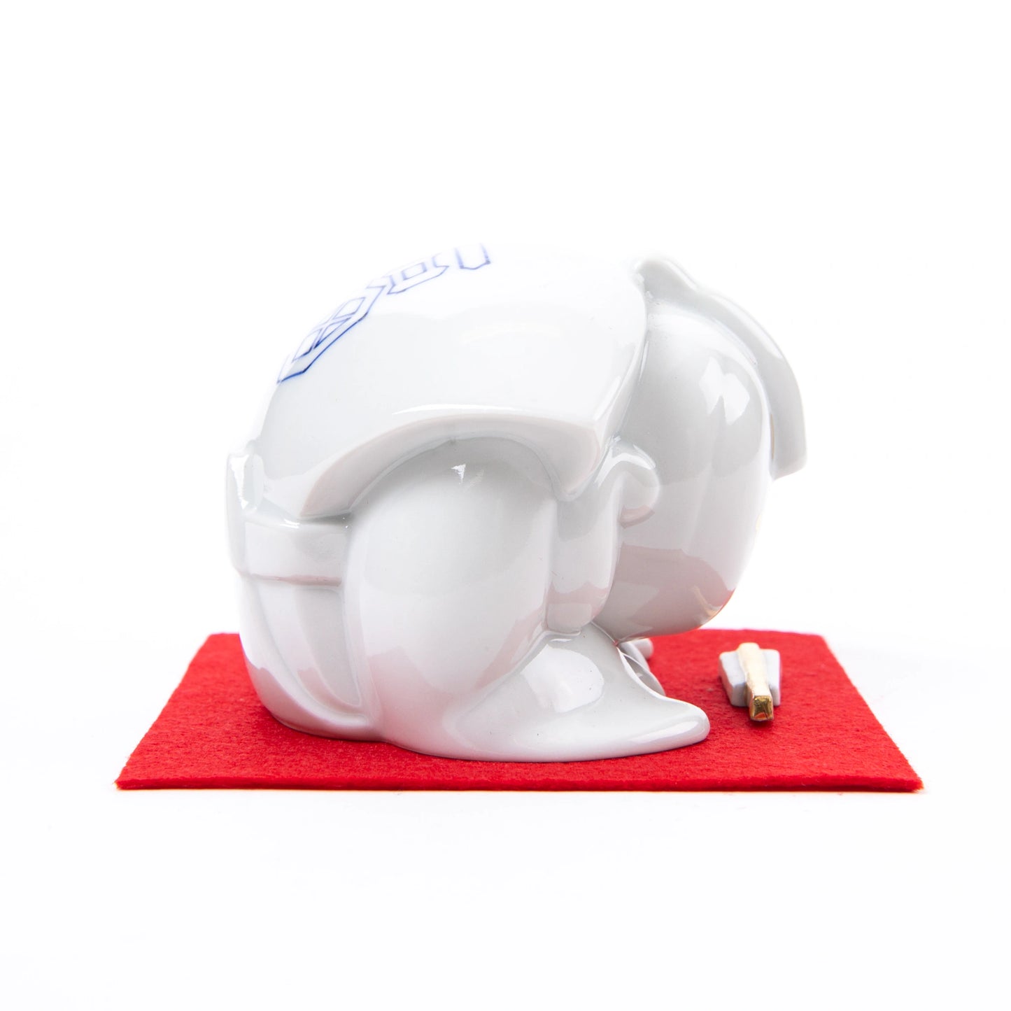 Side view of the Fukusuke Sometsuke doll, fully dressed in white with delicate gold facial features, bowing on a red mat with a decorative paper talisman.