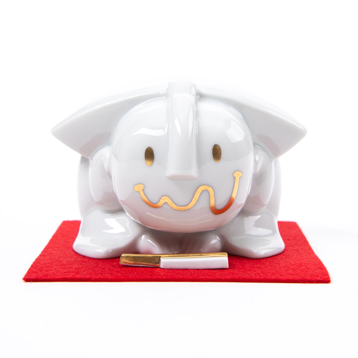 Front view of the Fukusuke Sometsuke doll, showcasing its minimalist gold smile and eyes, placed on a red mat with a paper talisman.