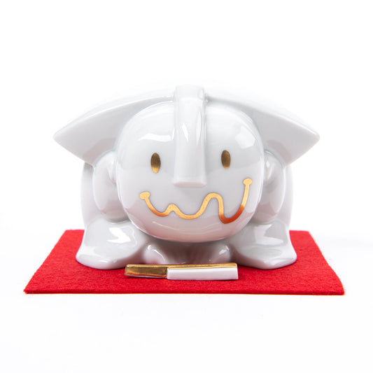 Front view of the Fukusuke Sometsuke doll, showcasing its minimalist gold smile and eyes, placed on a red mat with a paper talisman.