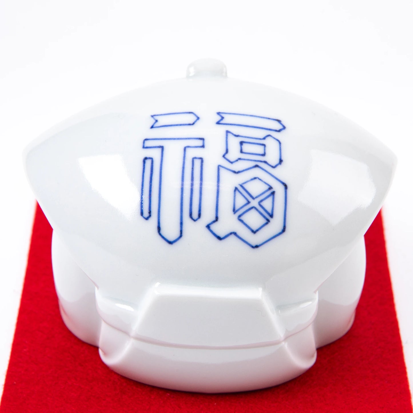 Close-up of the back of the Fukusuke Sometsuke doll, featuring the character "fuku" (fortune) in blue, painted on a white ceramic surface.