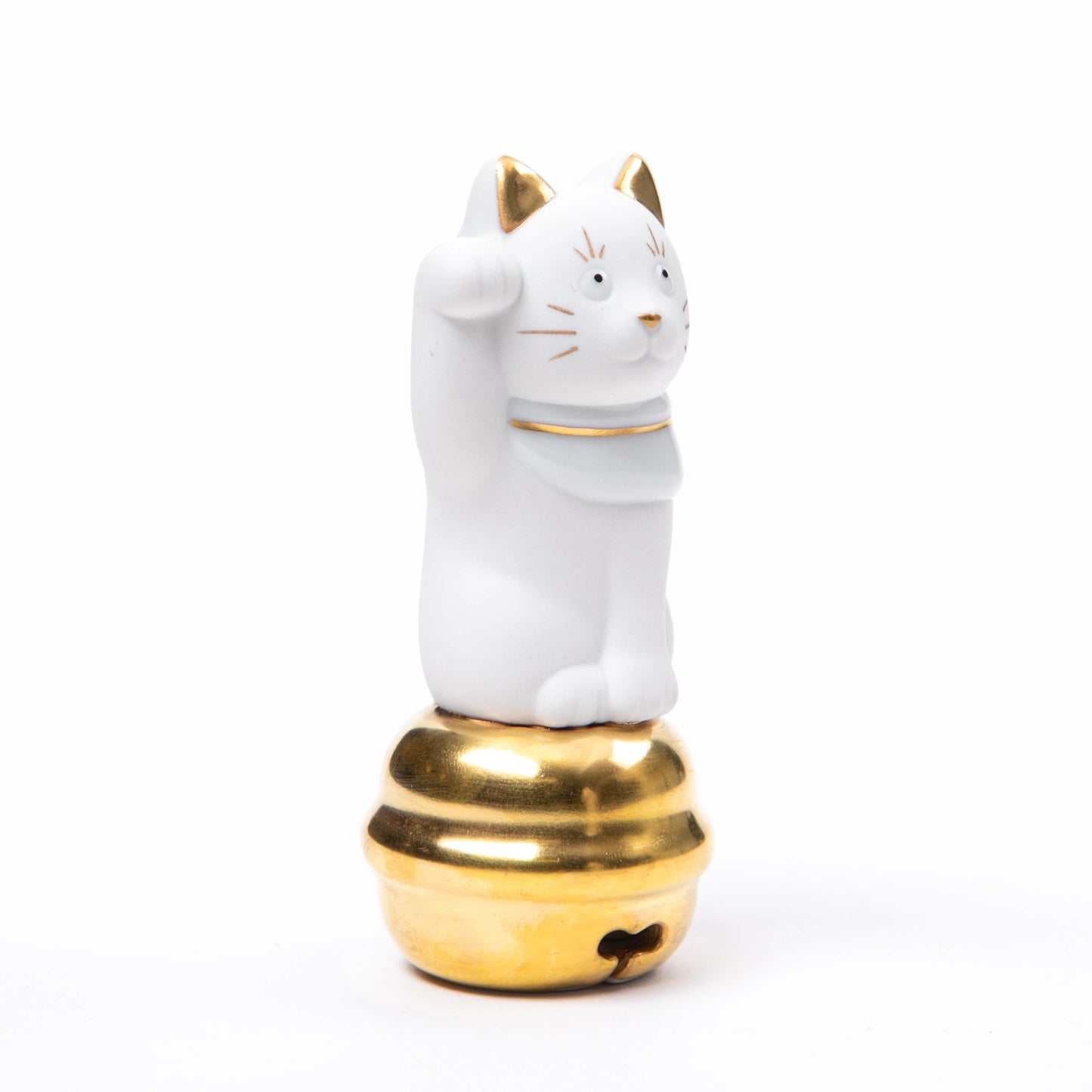 A white porcelain Maneki Neko figurine with gold accents, raising its right paw while sitting atop a polished golden bell.