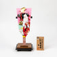 Traditional Dojoji-themed hagoita paddle featuring a 3D doll in red and mint kimono, displayed on a wooden base.