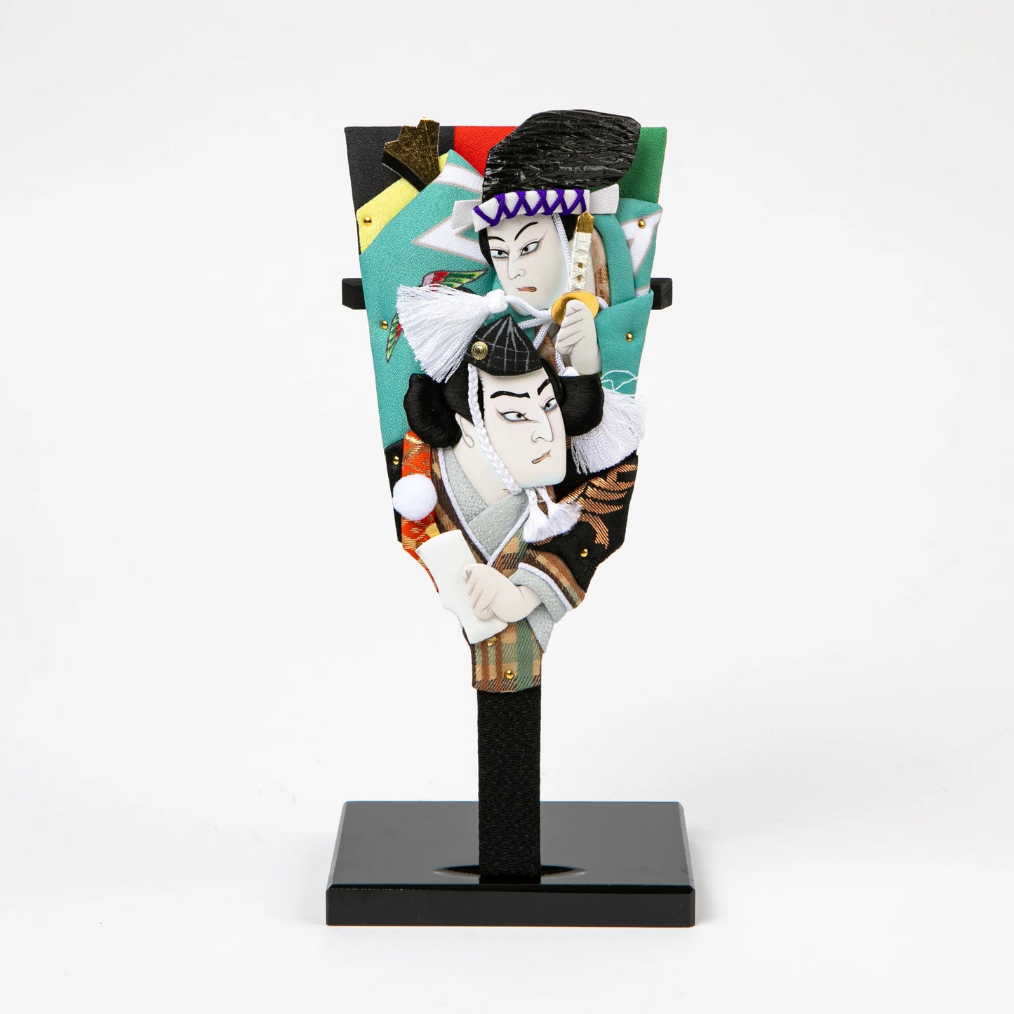 Decorative paddle featuring layered fabric reliefs of two kabuki actors in expressive poses, set against a vivid background.