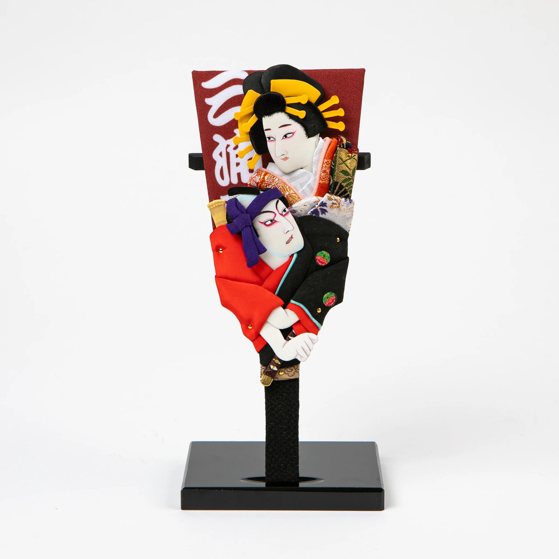 A decorative hagoita paddle featuring two Kabuki-style figures in traditional costume, mounted on a black base.