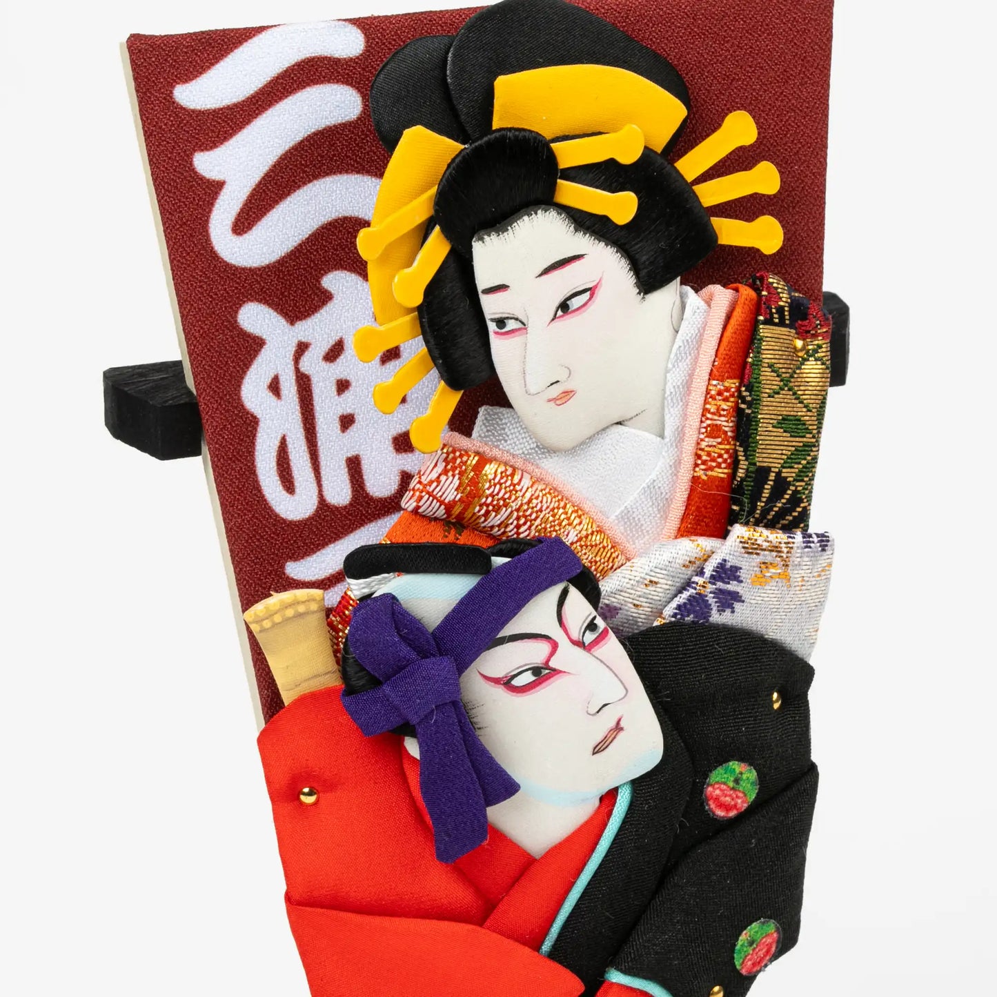 A close-up of the Kabuki-themed hagoita paddle, highlighting the expressive embroidered faces and vibrant fabric details of the two characters.