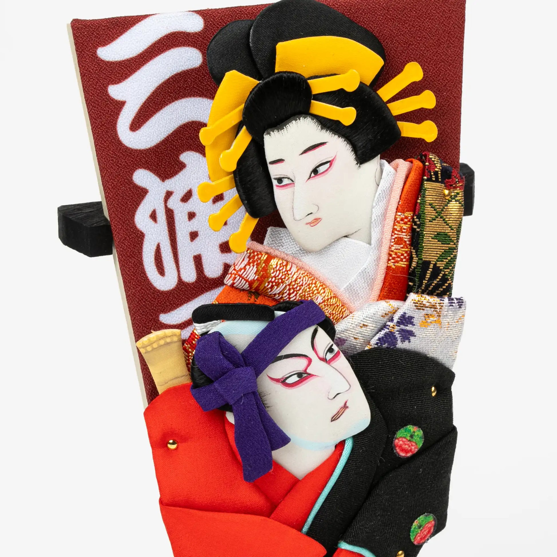 A close-up of the Kabuki-themed hagoita paddle, highlighting the expressive embroidered faces and vibrant fabric details of the two characters.