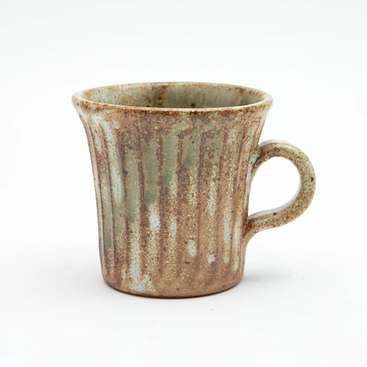 A Shigaraki ware mug by Hinomigama with vertical ribbed grooves, a kohiki white slip base and vidro ash glaze in soft sage and celadon tones over a warm iron rich clay body, set against a white background.