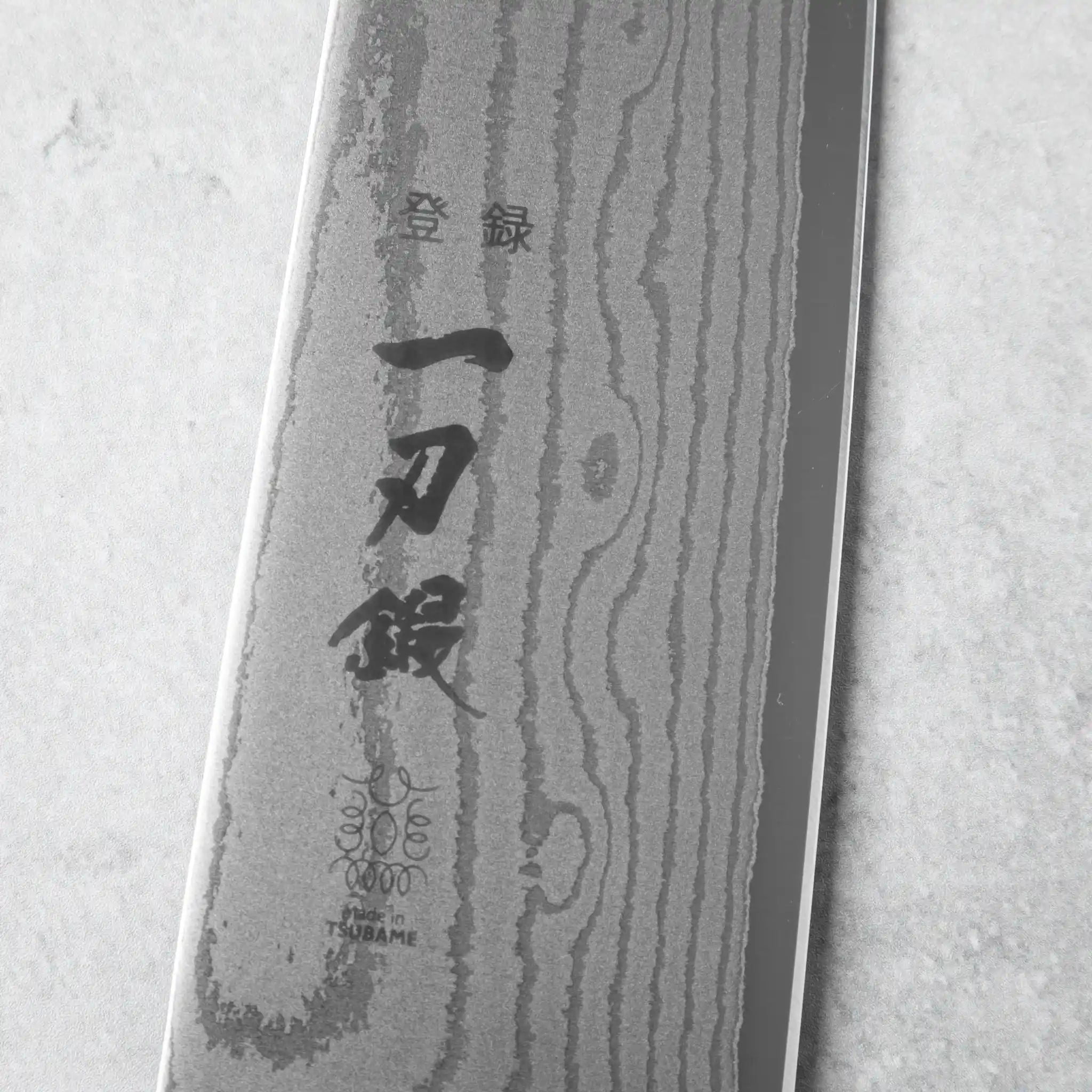 The tip of the chef’s knife, showcasing the fine tapering and polished Damascus layers.