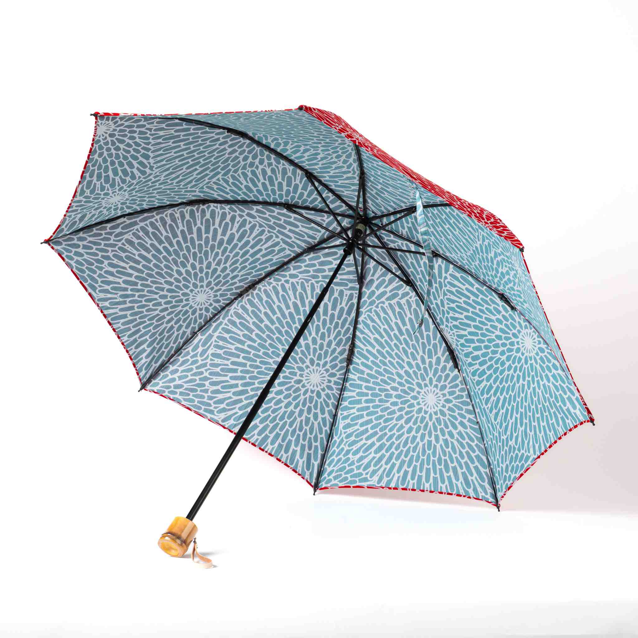 Isa Moyō Folding Umbrella opened, revealing the Chrysanthemum motif on a light blue background, with the bamboo handle visible.