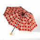 Isa Moyō Folding Umbrella opened, revealing the Pine Tree motif on a red background, with the bamboo handle visible.