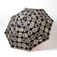 Isa Moyō Folding Umbrella fully opened, showcasing the intricate Pine Tree motif against a dark navy  background.
