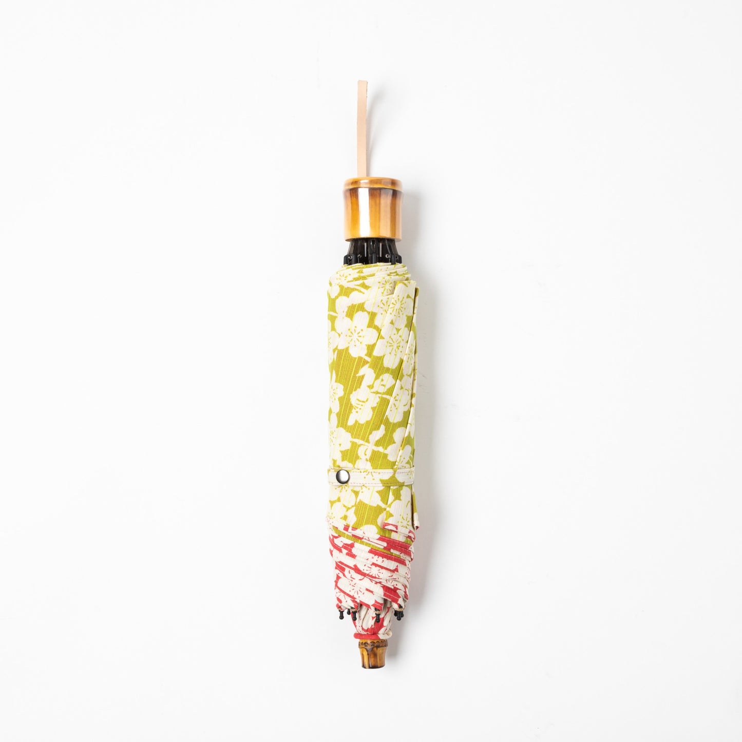 Isa Moyō Folding Umbrella in its compact, folded state, highlighting the bamboo handle and the contrast between the outer red fabric and inner light green lining.