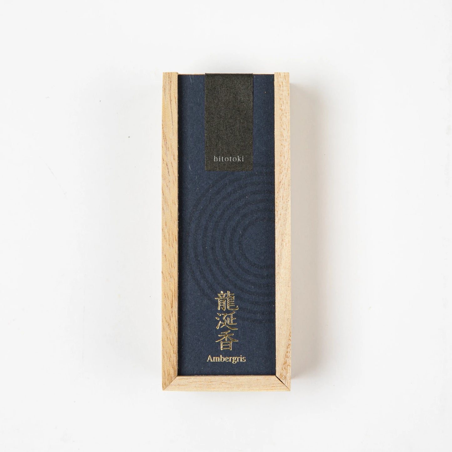 A dark blue "hitotoki" incense box labeled "Ambergris" with gold Japanese text, displayed vertically on a white background.