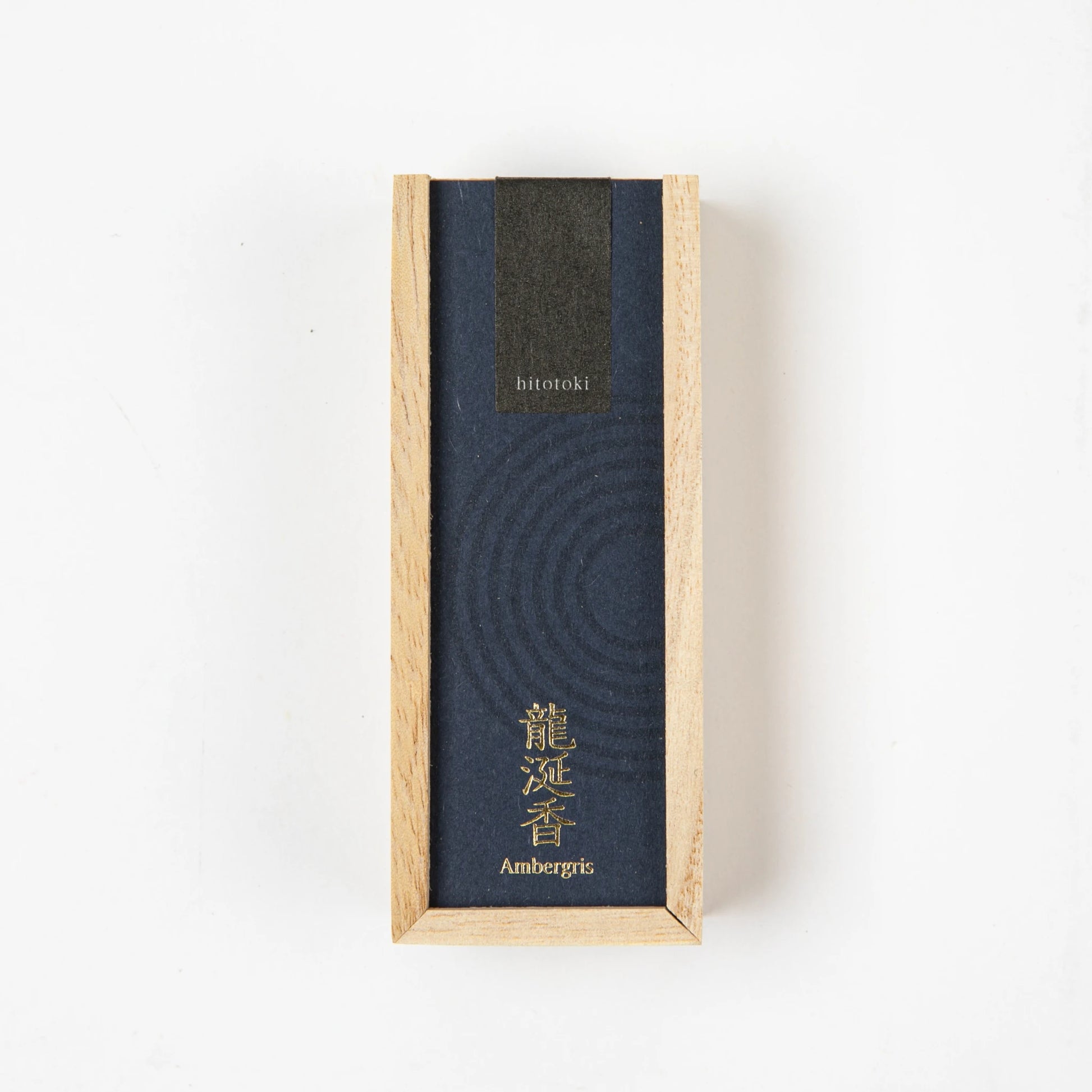 A dark blue "hitotoki" incense box labeled "Ambergris" with gold Japanese text, displayed vertically on a white background.