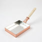 Angled view of a rectangular copper tamagoyaki pan showing its smooth interior and pale wooden handle.
