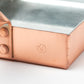 Close-up of the copper corner of a tamagoyaki pan, featuring rivets and a stamped Nabemura logo.