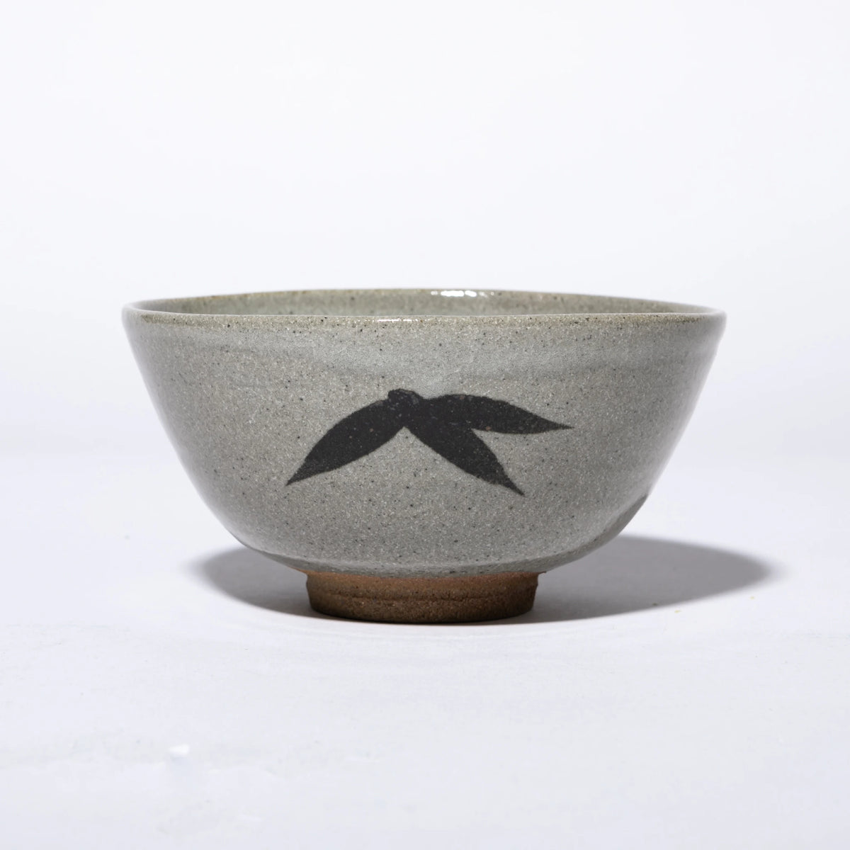 Front view of the Nakazato Tarouemon E-Karatsu matcha bowl with bamboo motif, showing a wide deep form with pale grey feldspathic glaze, a dense iron-oxide bamboo leaf cluster on the exterior wall, and an unglazed sandy clay foot ring.