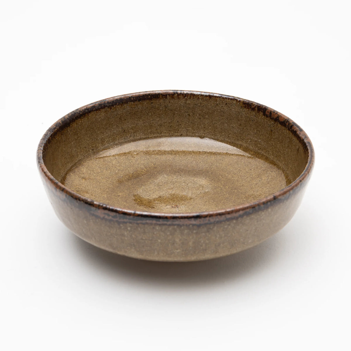 Three-quarter view of the Nakazato Tarouemon Yellow Karatsu mukozuke serving dish, showing a round open form with warm ochre ash glaze across the interior deepening to near-black at the thickened rim.