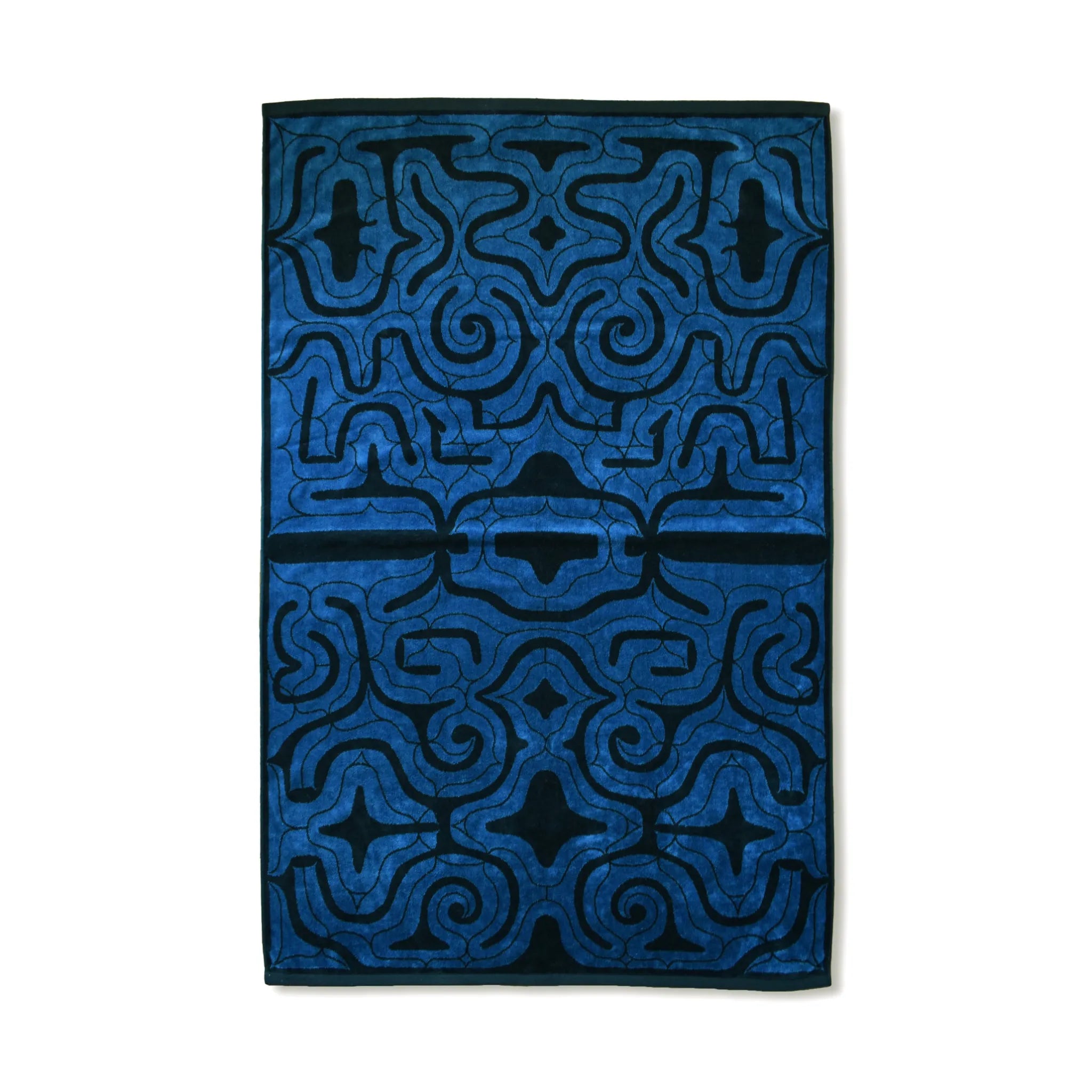 Front view of the Nibutani Works Ainu pattern Imabari towel blanket in blue and navy, showing a symmetrical kaparamip pattern of morew-noka spirals and ay-us-noka thorn forms across the full surface with a dark navy border.