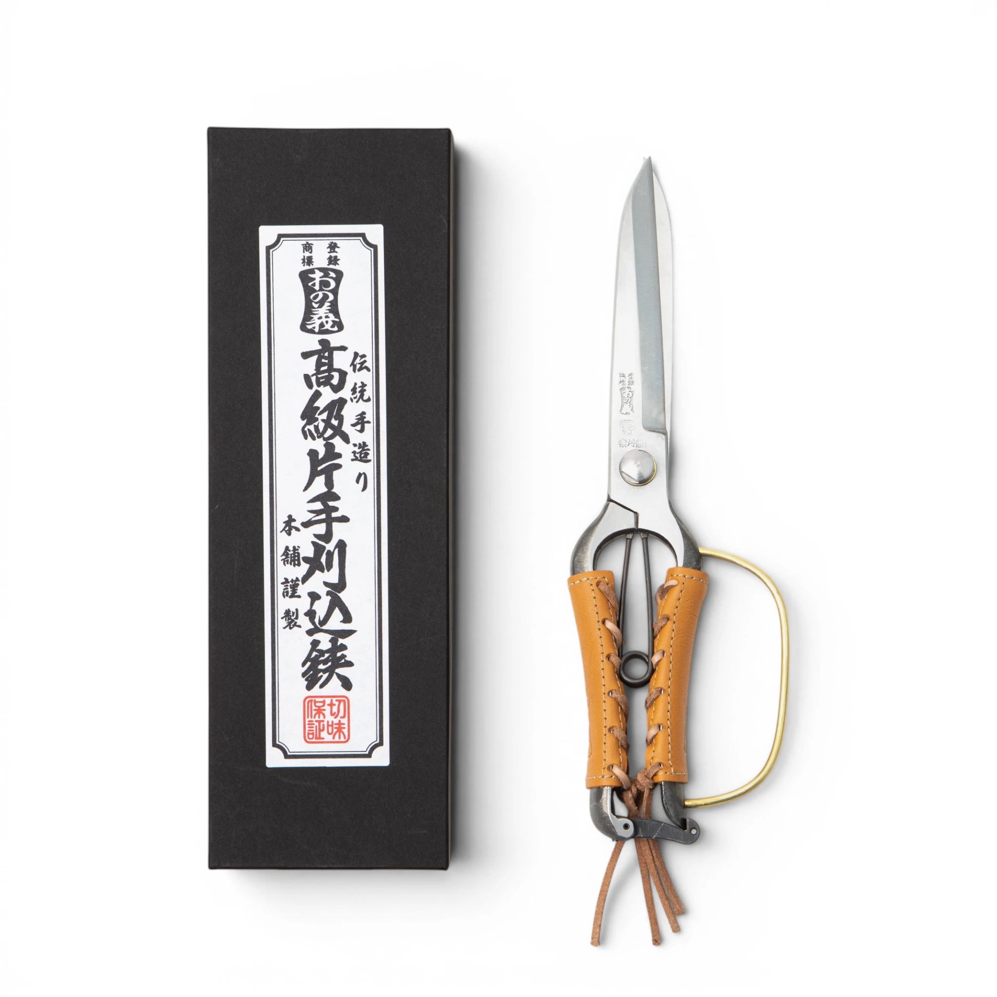 Front view of Onoyoshi Hamono one-hand hedge shears with brass guard and camel leather grip covers laced at the seam, alongside the branded black presentation box.