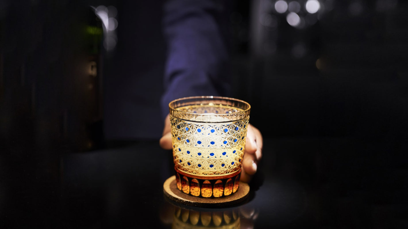 Hand offering an Edo Kiriko Glass forward against a dark background