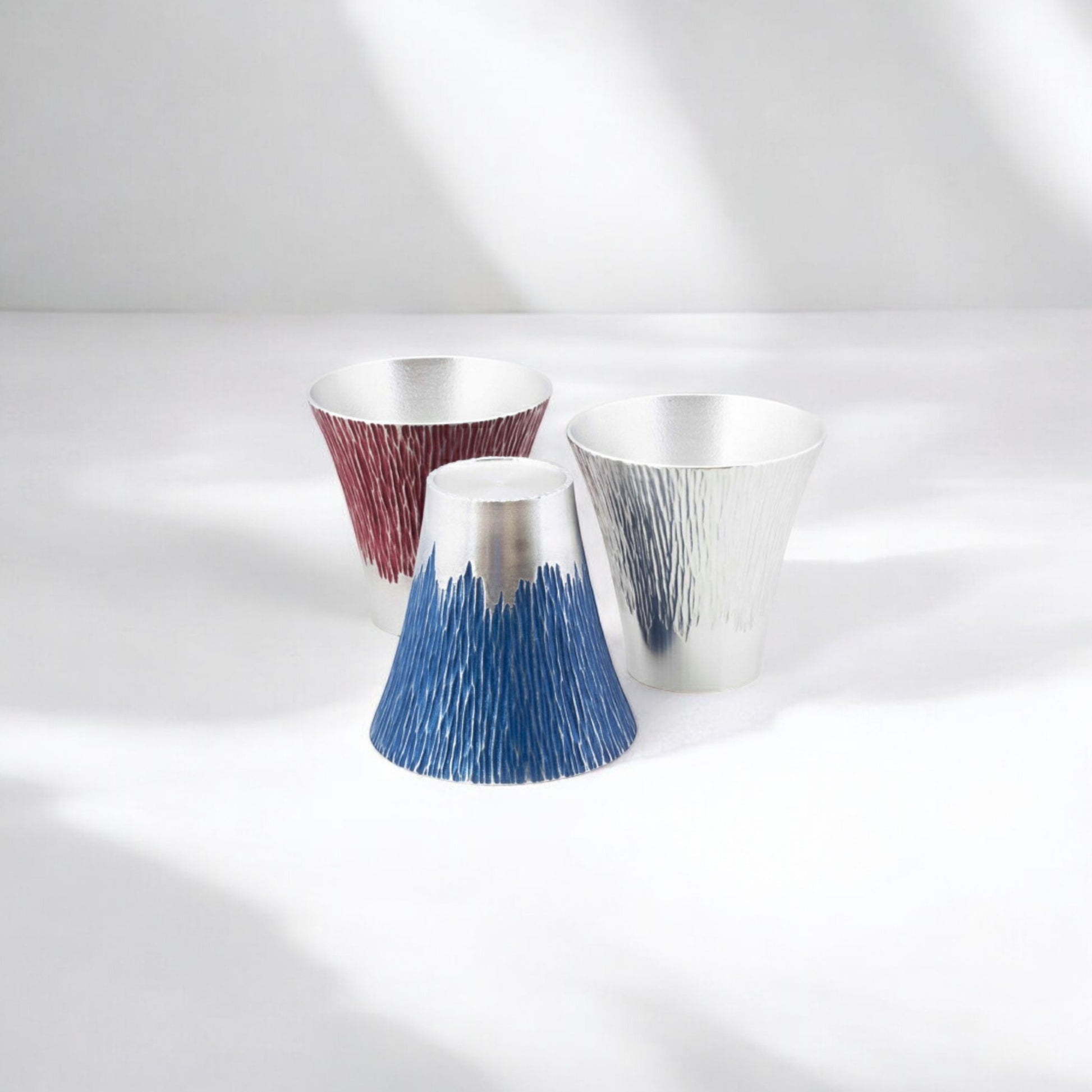 Three Osaka Suzuki Mt. Fuji Tumblers, displayed in red, blue, and silver variations, with a textured design resembling the iconic mountain, highlighting Japanese artistry in metalwork.
