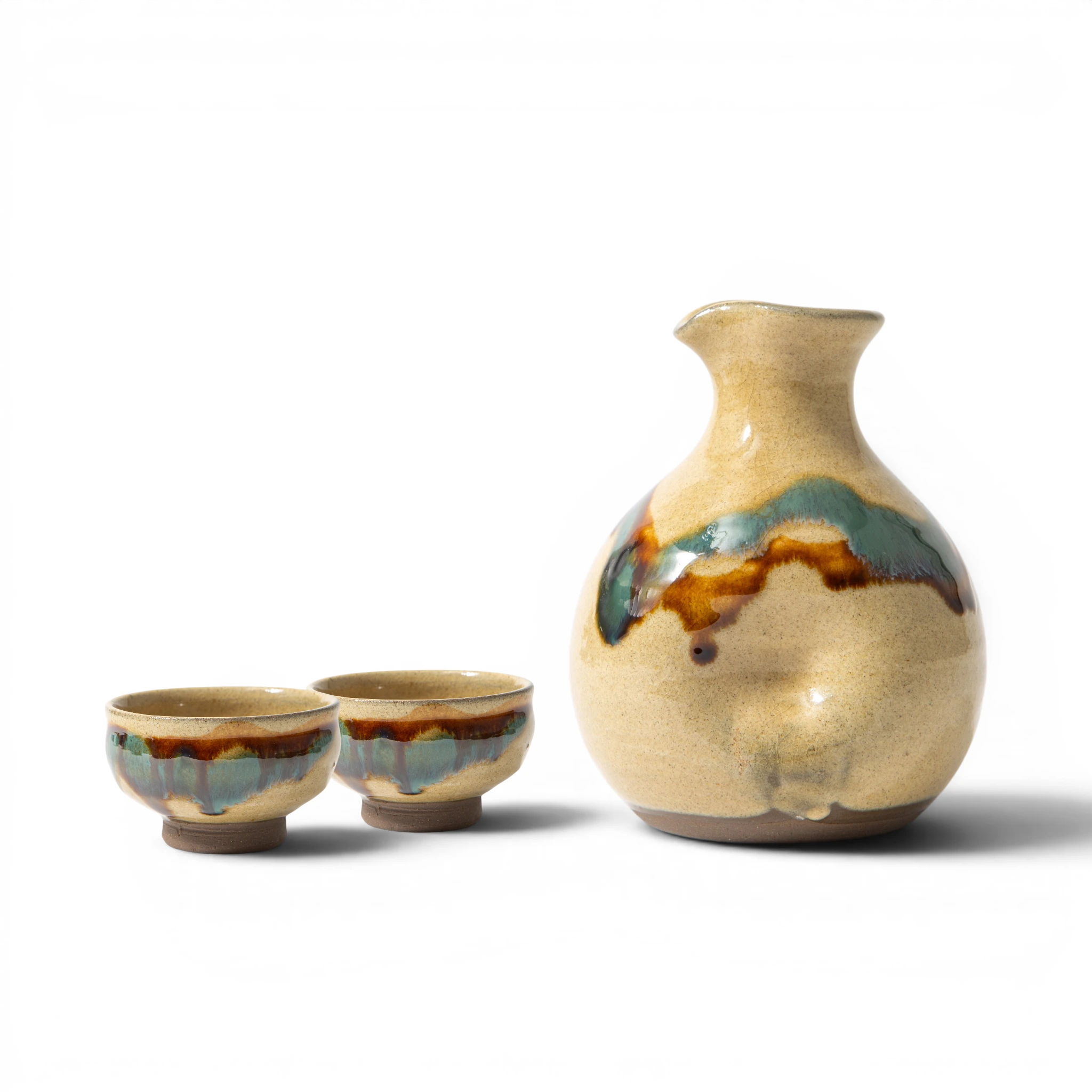 Front view of a Ryumonji Yaki sansai glaze sake set, showing a rounded tokkuri with amber, teal, and dark iron glaze breaking across the shoulder, alongside 2 small guinomi with the same three-color glaze dripping from the rim.
