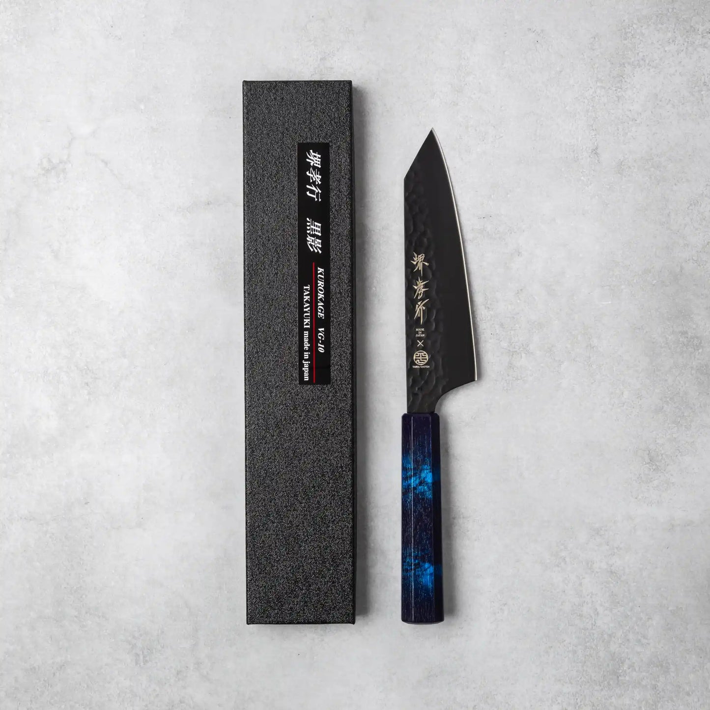 Sakai Takayuki Kurokage VG10 Kengata Santoku Knife with a vibrant blue octagonal handle, displayed next to its sleek black packaging featuring Japanese characters and branding