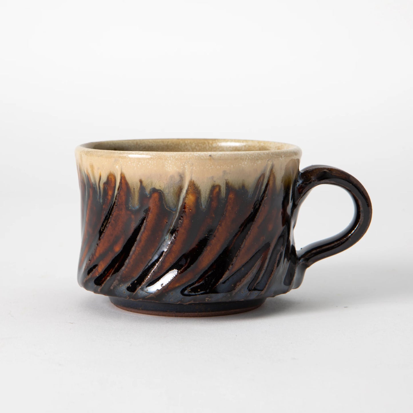 A wide, low Tamba ware mug by Shozo Gama with diagonal hand carved facets, a deep amber and iron brown glaze on the lower body transitioning to pale stone at the rim, and a dark loop handle, photographed against a white background.