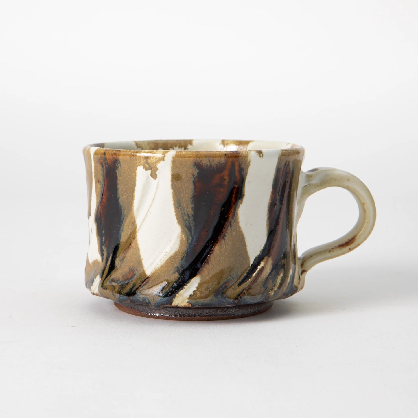 A wide, low Tamba ware mug by Shozo Gama with diagonal hand carved facets covered in layered ash glaze in honey, sandy earth, white, and deep iron brown tones, with a pale loop handle, photographed against a white background.