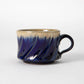 A wide, low Tamba ware mug by Shozo Gama with diagonal hand carved facets, a deep lapis blue glaze on the lower body transitioning to pale cream at the rim, and a dark loop handle, photographed against a white background.