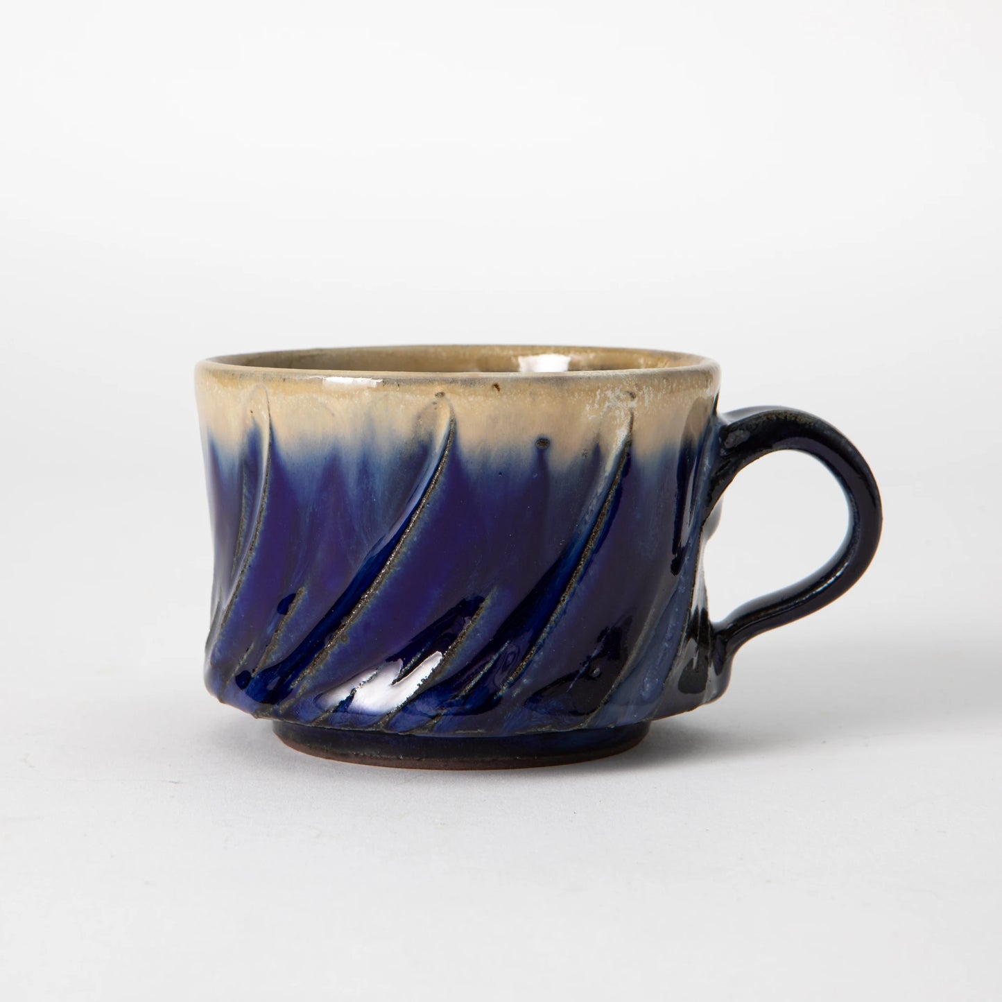 A wide, low Tamba ware mug by Shozo Gama with diagonal hand carved facets, a deep lapis blue glaze on the lower body transitioning to pale cream at the rim, and a dark loop handle, photographed against a white background.