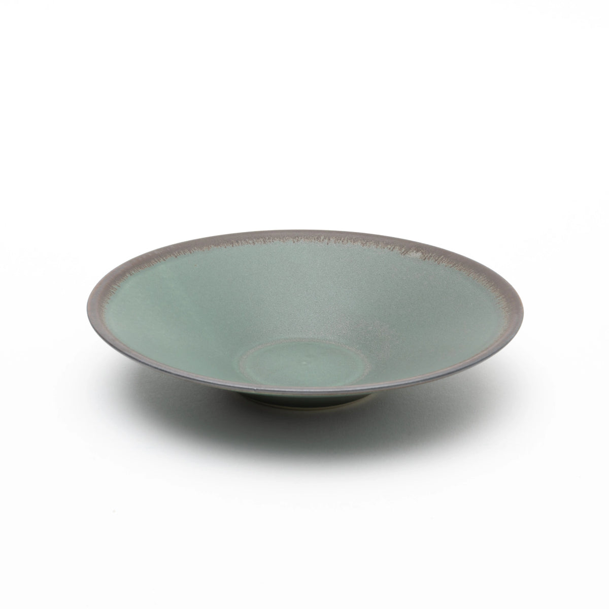 Three-quarter view of the Tsukamoto Mashiko ware SABI flat bowl medium in deep green, showing a wide shallow form with a matte, vintage-finish glaze across the interior and dark clay body visible at the rim edge.
